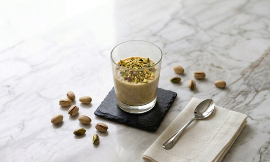 Pistazien-Panna Cotta mit Nocissimo Pistaziencreme nach unserem Rezept, serviert in einem Dessertglas und dekoriert mit fein gehackten Pistazien.
